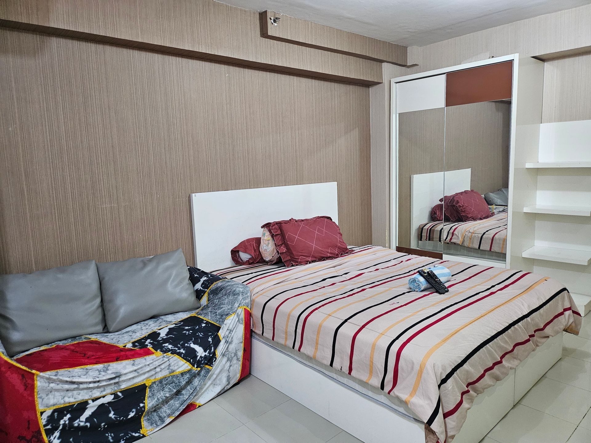 Bedroom with striped bedspread, mirrored wardrobe, and small couch with patterned cover.