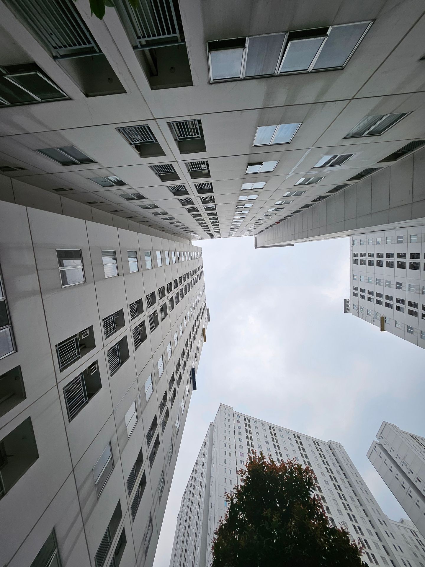 Upward view of tall residential buildings forming a narrow alley against a cloudy sky.